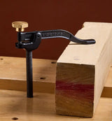Veritas woodworking hold down clamp holding a piece of wood on a wooden bench with a brown background