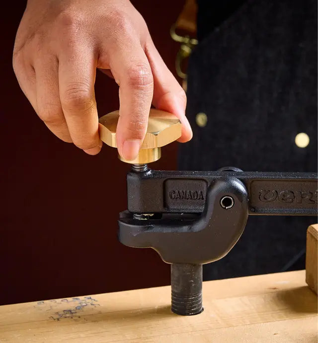 Woodworker adjusting hold down clamp by turning brass adjuster handle. 